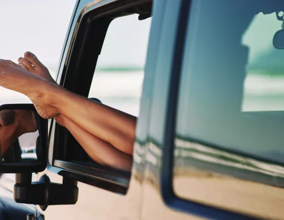 Persona sacando los pies por la ventana del conductor de un coche estacionado