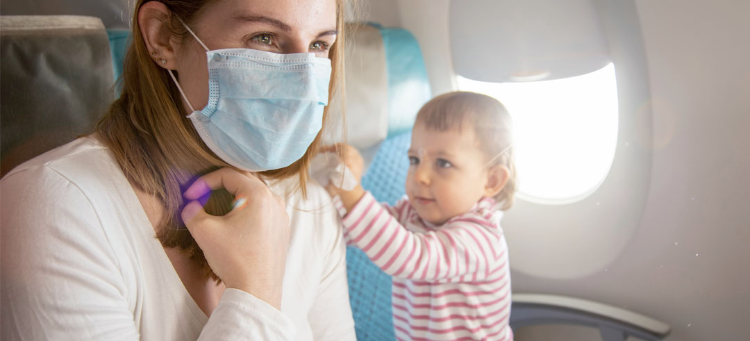 Mujer con mascarilla sentada en un avión mientras un bebé intenta jugar con ella